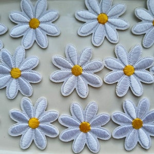 May include: White daisy flower patches with yellow centres. These embroidered appliques feature detailed stitching and are ideal for adding a floral touch to clothing, accessories, or craft projects. The patches are approximately 5 cm in diameter.