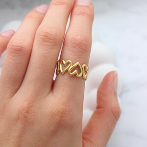 Peut inclure: Une bague dor&eacute;e orn&eacute;e d'une s&eacute;rie de c&oelig;urs ajour&eacute;s. La bague est port&eacute;e au doigt, mettant en valeur son design d&eacute;licat. La teinte chaude de la bague contraste avec le teint de la peau, soulignant l'attrait esth&eacute;tique du bijou.