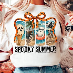 May include: White long-sleeved sweatshirt with a colorful graphic of spooky summer scenes. The design includes a ghost ice cream cone, a skeleton holding a drink, and the words "SPOOKY SUMMER" in black block letters.