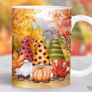 May include: White ceramic mug with a fall-themed design featuring three gnomes with red, green, and yellow hats. The gnomes are standing in a forest with orange, yellow, and red leaves. The mug has a white handle.