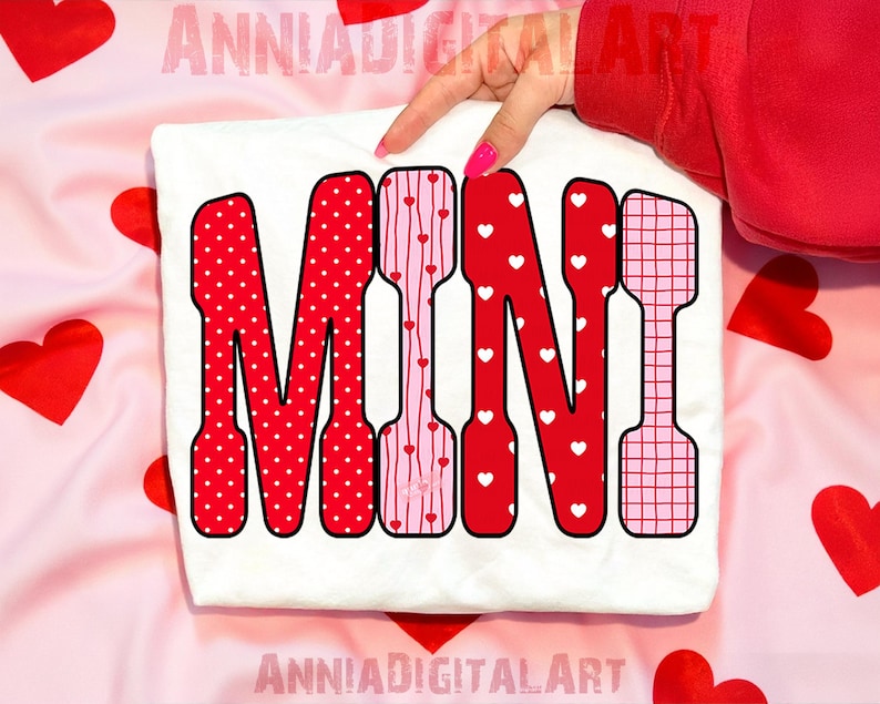 May include: A white t-shirt with the word "MINI" in a bold, decorative font. The letters are red and pink, featuring polka dots, stripes, and heart patterns. The background is a pink fabric with red heart shapes.