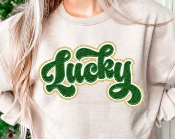 May include: A beige sweatshirt with a green and gold "Lucky" graphic.