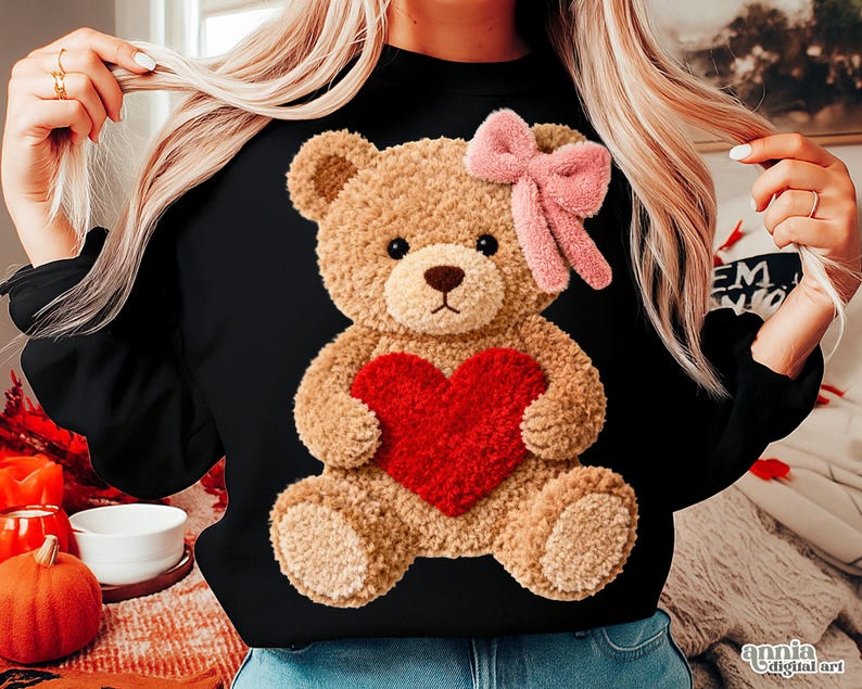 May include: Black long-sleeved sweatshirt featuring a plush teddy bear holding a red heart. The teddy bear has a pink bow and is centered on the front. The sweatshirt is a solid black color.