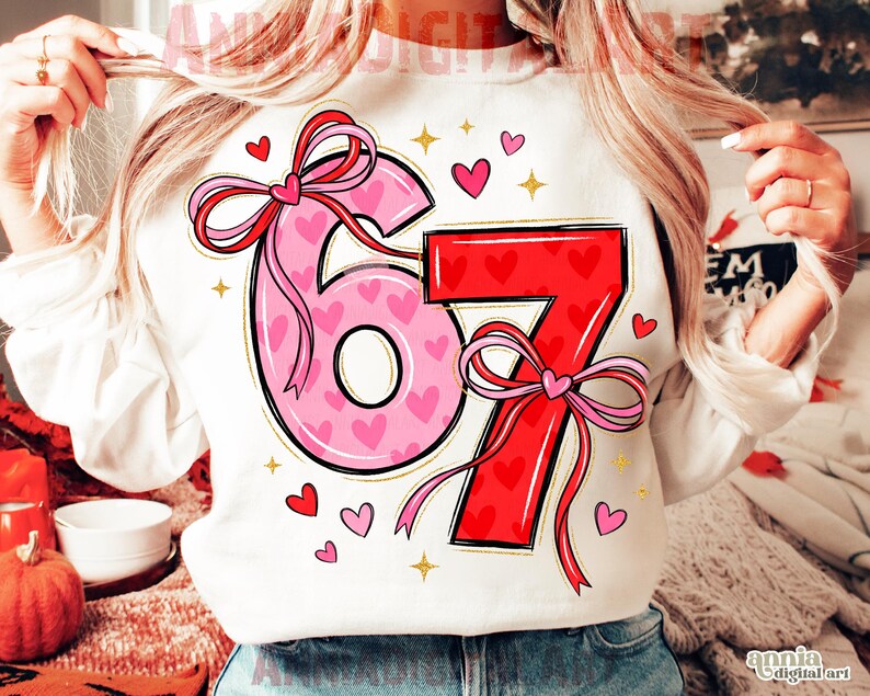 May include: White sweatshirt with the numbers "67" in pink and red, decorated with hearts and bows. The number "6" is pink with small pink hearts, and the number "7" is red with red hearts. Gold stars and small hearts are scattered around the numbers.