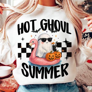 May include: White sweatshirt with a Halloween-themed graphic. The design features a ghost wearing sunglasses on a pink flamingo float, pumpkins, and the words "HOT GHOUL SUMMER" in black. Bats and stars complete the design.