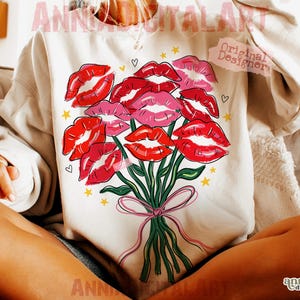 May include: Cream-colored sweatshirt featuring a bouquet of red and pink lips with green stems and a pink bow. The design includes small yellow stars and hearts. The words "ANNIA DIGITAL ART" and "Original Designer" are visible.