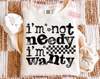 May include: Cream-colored sweatshirt with the text "I'm not needy I'm wanty" in black. The design includes stars and a checkered pattern. The sweatshirt has a crew neck and long sleeves.