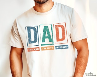 May include: White t-shirt with a vintage-style graphic that reads "DAD" in colorful boxes. The boxes are labeled "The Man", "The Myth", and "The Legend".