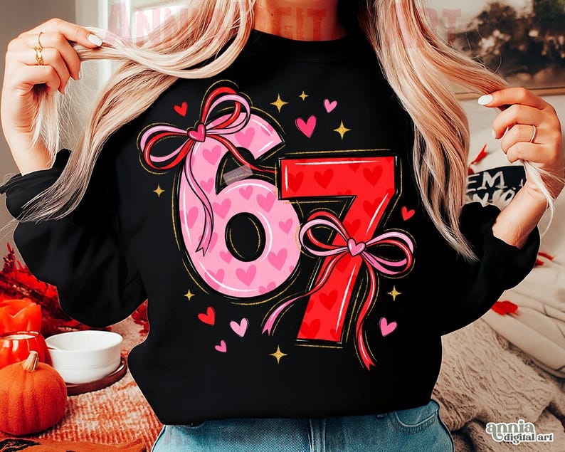 May include: Black sweatshirt featuring the numbers "67" in a pink and red design. The number "6" is pink and filled with small hearts, while the "7" is red. Both numbers have bow accents. Small hearts and stars surround the numbers.