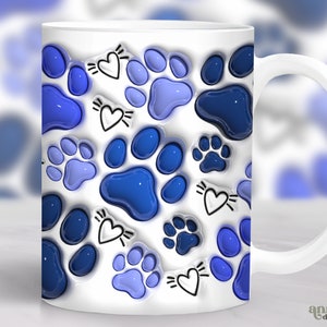 Op de afbeelding: Witte keramische mok met een herhalend patroon van blauwe pootafdrukken en zwart-witte harten. De pootafdrukken variëren in blauwtinten, waardoor een 3D-effect ontstaat. De mok heeft een wit oor en een glanzende afwerking.