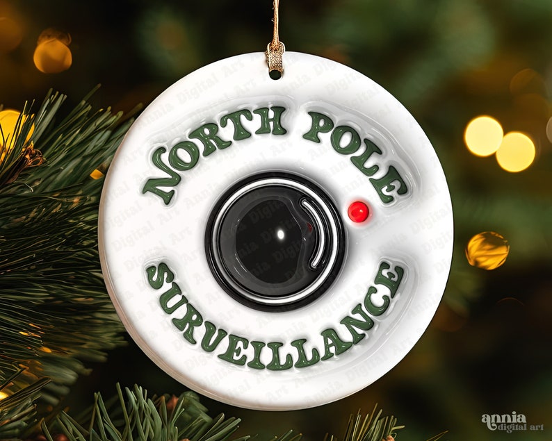 May include: White round Christmas ornament with green text that reads "North Pole Surveillance" and a black and white camera graphic with a red light.
