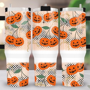 May include: A set of three white travel mugs with a Halloween-themed design. The design features orange jack-o'-lanterns, green leaves, and a black and white checkered pattern. The mugs have black handles and lids.