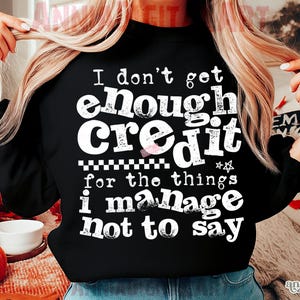 May include: Black crew neck sweatshirt with the text "I don't get enough credit for the things I manage not to say" in white. The sweatshirt has a checkered pattern and star graphic.