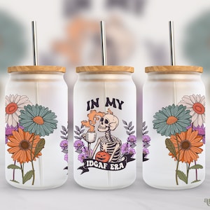 May include: Three white tumblers with lids and straws. The center tumbler has a black and white skeleton graphic with the text "In My IDGAF Era". The tumblers have a floral design with orange, purple, and blue flowers.