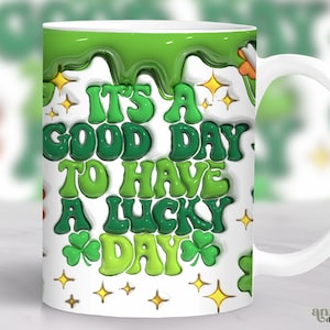 May include: White ceramic mug with a green, white and gold design. The mug has a handle and features the text "It's a good day to have a lucky day".
