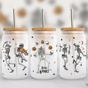 May include: Three frosted glass tumblers with bamboo lids and metal straws. Each tumbler features a different design of skeletons with Halloween-themed elements like pumpkins, stars, and a crescent moon. The middle tumbler has the text "Stay Spooky" printed on it.