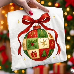 Może przedstawiać: Biała kwadratowa tkanina z motywem bombki choinkowej. Ozdoba jest czerwona, zielona i złota z czerwoną wstążką. Wzór ozdoby zawiera choinkę, płatki śniegu i prezent. Złote gwiazdki zdobią ozdobę.