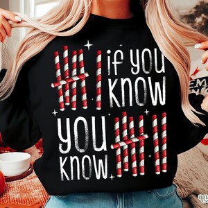 May include: Black sweatshirt with the text "If you know, you know" in white. The design includes red and white striped candy cane-like graphics. The sweatshirt is a festive holiday-themed apparel item.