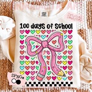 May include: Cream-colored sweatshirt with the text "100 days of school" and a pink pencil-shaped bow. The bow is surrounded by colorful hearts. A black and white checkered pattern is at the bottom of the design.