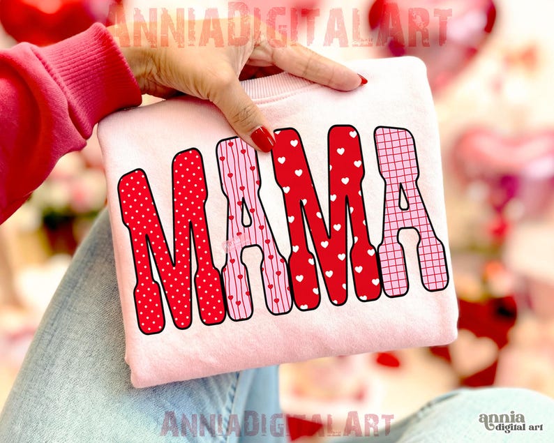 May include: A light pink sweatshirt with the word "MAMA" in red and pink letters. The letters are decorated with polka dots, hearts, and a grid pattern. The sweatshirt is held by a person.