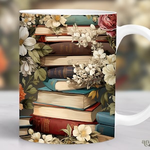 Op de afbeelding: Een witte keramische mok met een kleurrijk ontwerp met een stapel vintage boeken versierd met delicate witte bloemen en groene bladeren. De mok heeft een witte handgreep.