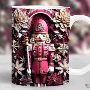 May include: White ceramic mug with a pink and gold design featuring a nutcracker standing in front of a floral pattern. The nutcracker is wearing a red and gold uniform with a white hat.