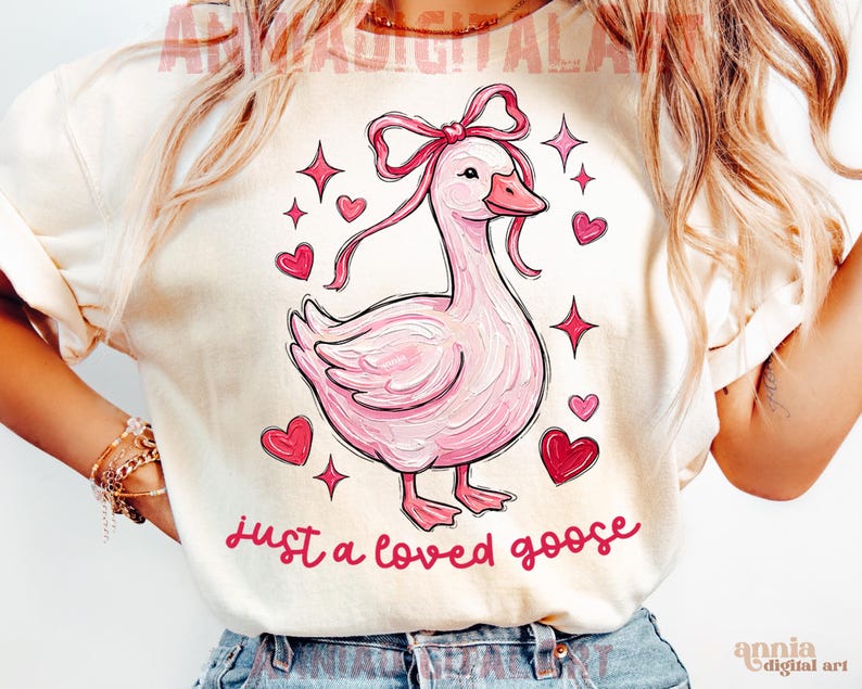 Pu&ograve; includere: T-shirt color crema con un'illustrazione di un'oca rosa con un fiocco, circondata da cuori e stelle. Il testo "just a loved goose" &egrave; scritto in corsivo. Un design carino e stravagante.