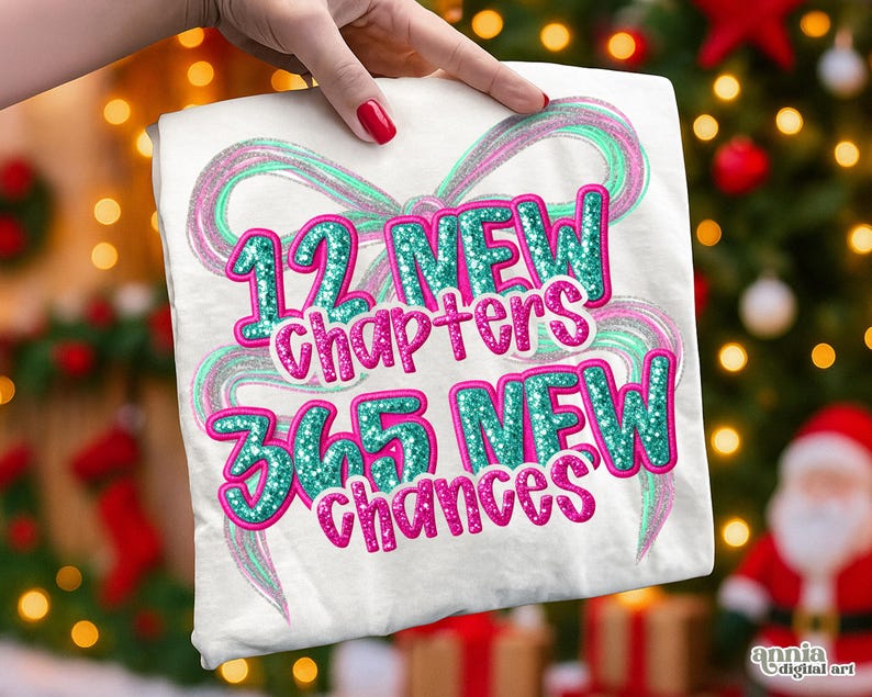 May include: White t-shirt with the text "12 NEW chapters 365 NEW chances" in teal and pink glitter. The design includes a teal and pink ribbon-like graphic. The shirt is held up by a hand with red nail polish.