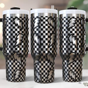 May include: Three stainless steel travel mugs with black handles and white lids. The mugs feature a black and white checkered pattern with silver lightning bolt designs. The mugs are designed for hot or cold beverages.