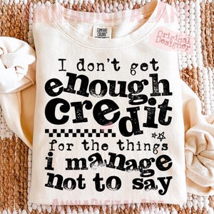 May include: Cream-colored sweatshirt with the text "I don't get enough credit for the things I manage not to say" in black. The sweatshirt has a crew neck and long sleeves. The text is in a bold, playful font.