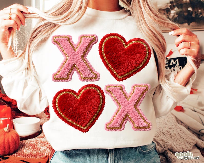 Op de afbeelding: Witte sweatshirt met roze en gouden "X" en rode hart patches. De patches hebben een fuzzy textuur en zijn goud omrand. Het ontwerp is gecentreerd op de voorkant van het shirt.