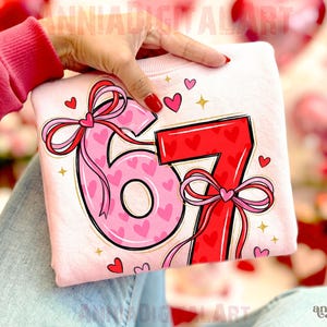 May include: A light pink sweatshirt featuring the numbers 6 and 7 in a decorative style. The number 6 is pink with heart patterns, and the number 7 is red. Both numbers have bows and are decorated with hearts and gold stars.