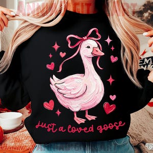 Pu&ograve; includere: Felpa nera con un disegno di un'oca rosa, completa di fiocco, cuori e stelle. La frase "just a loved goose" &egrave; scritta in rosa. Lo stile generale &egrave; stravagante e romantico, perfetto per l'abbigliamento casual.