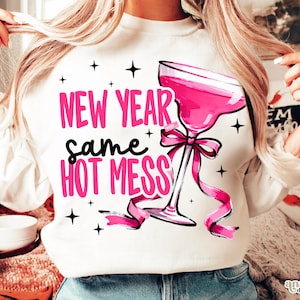 May include: White sweatshirt with the text "NEW YEAR same HOT MESS" in pink and black. A pink margarita glass with a ribbon is featured on the front, along with black star accents. The sweatshirt is a casual, festive garment.