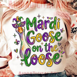 Op de afbeelding: Witte sweatshirt met een kleurrijke afbeelding van een gans met een Mardi Gras-masker en een narrenkap. De tekst "Mardi Goose on the Loose" is geschreven in groen, paars en geel. Het ontwerp bevat sterren, harten en fleur-de-lis.