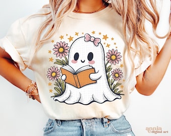 May include: A white t-shirt with a cute cartoon ghost reading a book. The ghost has pink flowers and stars around it. The text "annia digital art" is in the bottom right corner.