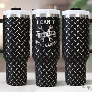 May include: Black stainless steel travel mug with a diamond plate pattern and a white lid. The mug has a black handle and the text "I CAN'T I HAVE PLANS IN THE GARAGE" in silver.