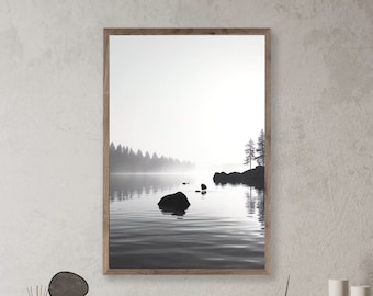 May include: Black and white photograph of a lake with a forest in the background. The lake is calm and still, with a few rocks in the foreground. The forest is silhouetted against the sky, and the sun is shining through the trees.