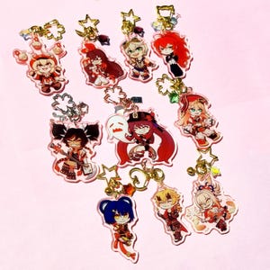 Pode incluir: Uma coleção de chaveiros de personagens em acrílico com figuras em estilo anime. Cada chaveiro tem um fecho dourado e um pingente em forma de estrela. As figuras são em várias cores, incluindo vermelho, azul e preto.