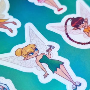 May include: A sticker sheet with illustrations of fairies from Pixie Hollow. The stickers show fairies with diverse hairstyles, clothing, and poses, set against a blue and green gradient background. The text "Pixie Hollow Sticker Sheet" is visible.
