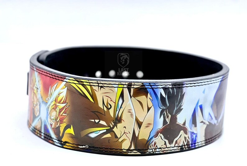 Puede incluir: Un cintur&oacute;n de levantamiento de pesas negro con un estampado de anime colorido con personajes de Dragon Ball Z. El cintur&oacute;n tiene una correa de cuero negro con costuras blancas y una hebilla plateada. El estampado presenta a Goku, Vegeta y otros personajes de la serie de anime.