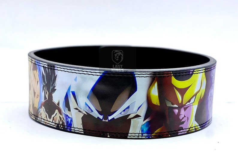 Puede incluir: Un cintur&oacute;n de cuero negro con un estampado de anime colorido que presenta personajes de Dragon Ball Z. El estampado incluye a Goku, Vegeta y Freezer.