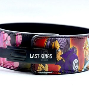 Puede incluir: Un cintur&oacute;n de levantamiento de pesas negro con un estampado de anime colorido que presenta personajes de Dragon Ball Z. El cintur&oacute;n tiene una hebilla de metal negro con las palabras "Last Kings" impresas en &eacute;l.