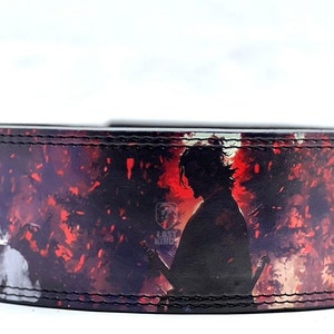 May include: A black leather belt with a red and white graphic print of a samurai warrior with a sword. The belt has a stitched edge.
