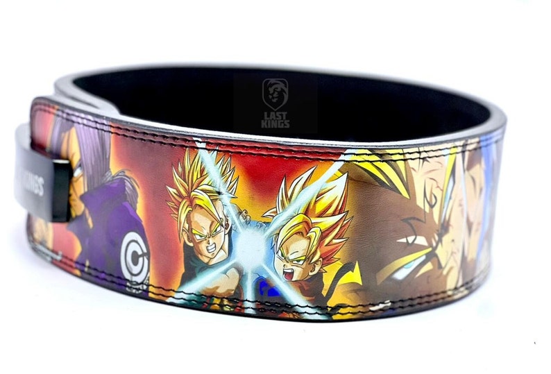 Puede incluir: Un cintur&oacute;n de levantamiento de pesas de cuero negro con un estampado colorido de personajes de anime de Dragon Ball Z. El cintur&oacute;n tiene el texto "Last Kings" en blanco.