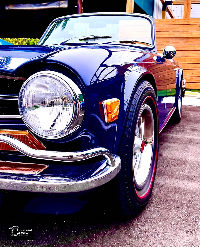 May include: A classic blue convertible car with chrome accents and a red stripe on the tyres. The car has a large, round headlight and a chrome bumper.