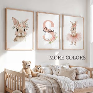 Peut inclure: Trois impressions d'art encadrées avec des illustrations à l'aquarelle. L'une montre un lapin avec une couronne florale, une autre porte le nom "Sophia" avec un motif floral, et la troisième représente un lapin en tutu. Le texte "MORE COLORS" est en dessous.