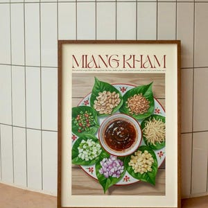 Puede incluir: Impresión enmarcada de Miang Kham, un aperitivo tailandés. La imagen muestra un plato con hojas de betel, cacahuetes, jengibre, lima, chalotas y una salsa sabrosa. El título "MIANG KHAM" se muestra en color granate.