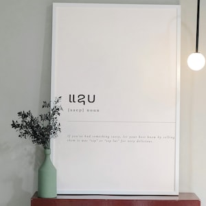 Könnte beinhalten: Ein weißer gerahmter Druck mit dem laotischen Wort "ແຊບ" (saep), das im Englischen "köstlich" bedeutet. Der Druck enthält auch die Definition des Wortes und eine Beschreibung, wie man es in der Konversation verwendet.