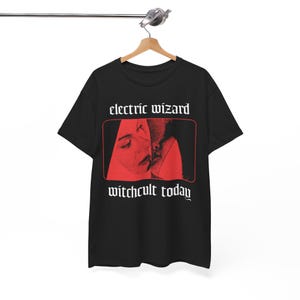May include: Black t-shirt with a red graphic featuring two faces and the text "electric wizard" above and "witchcult today" below. The t-shirt is hanging on a wooden hanger.